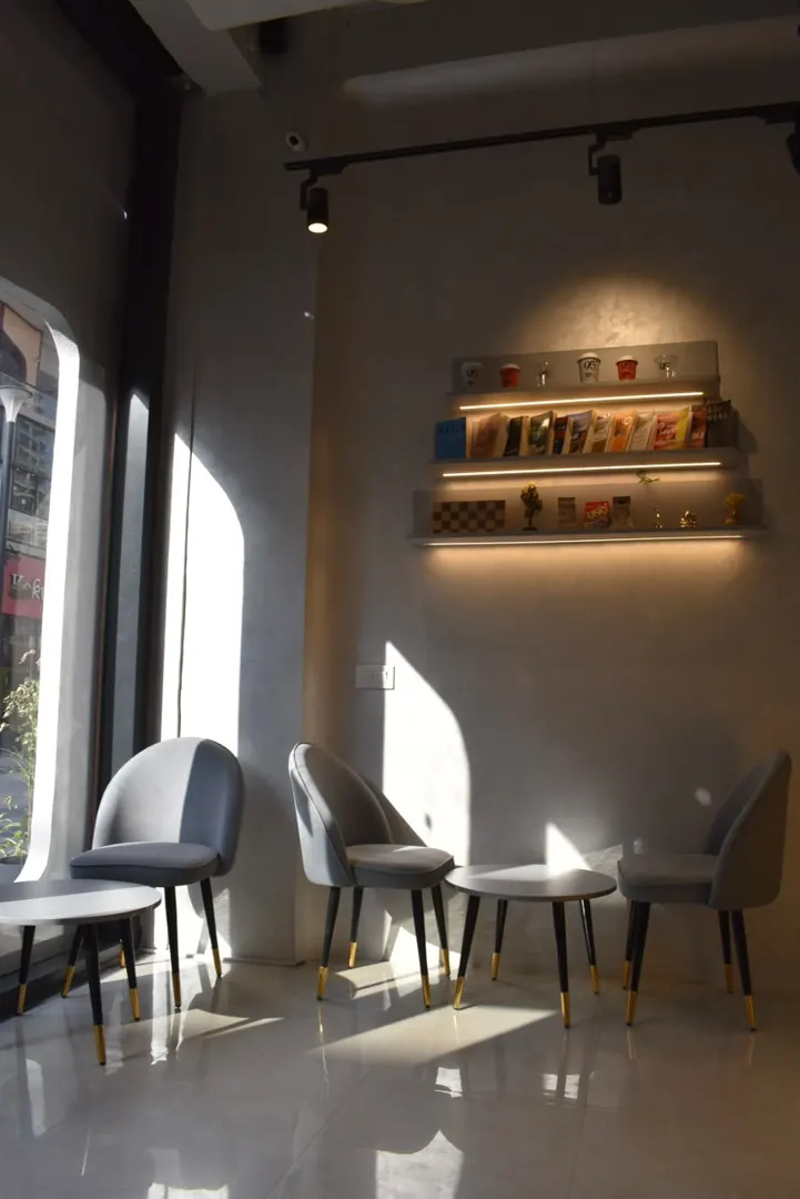 Grey velvet chairs by the window under the shelf lights