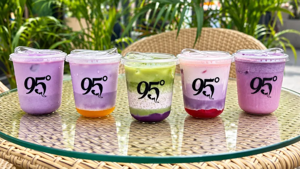 Five Ube Series drinks in 95 Degree cups on a glass table among plants